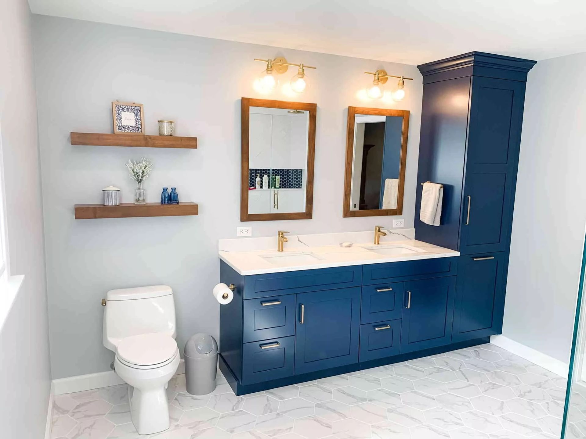 Bathroom remodel with navy double vanity, marble floor, and open shelving