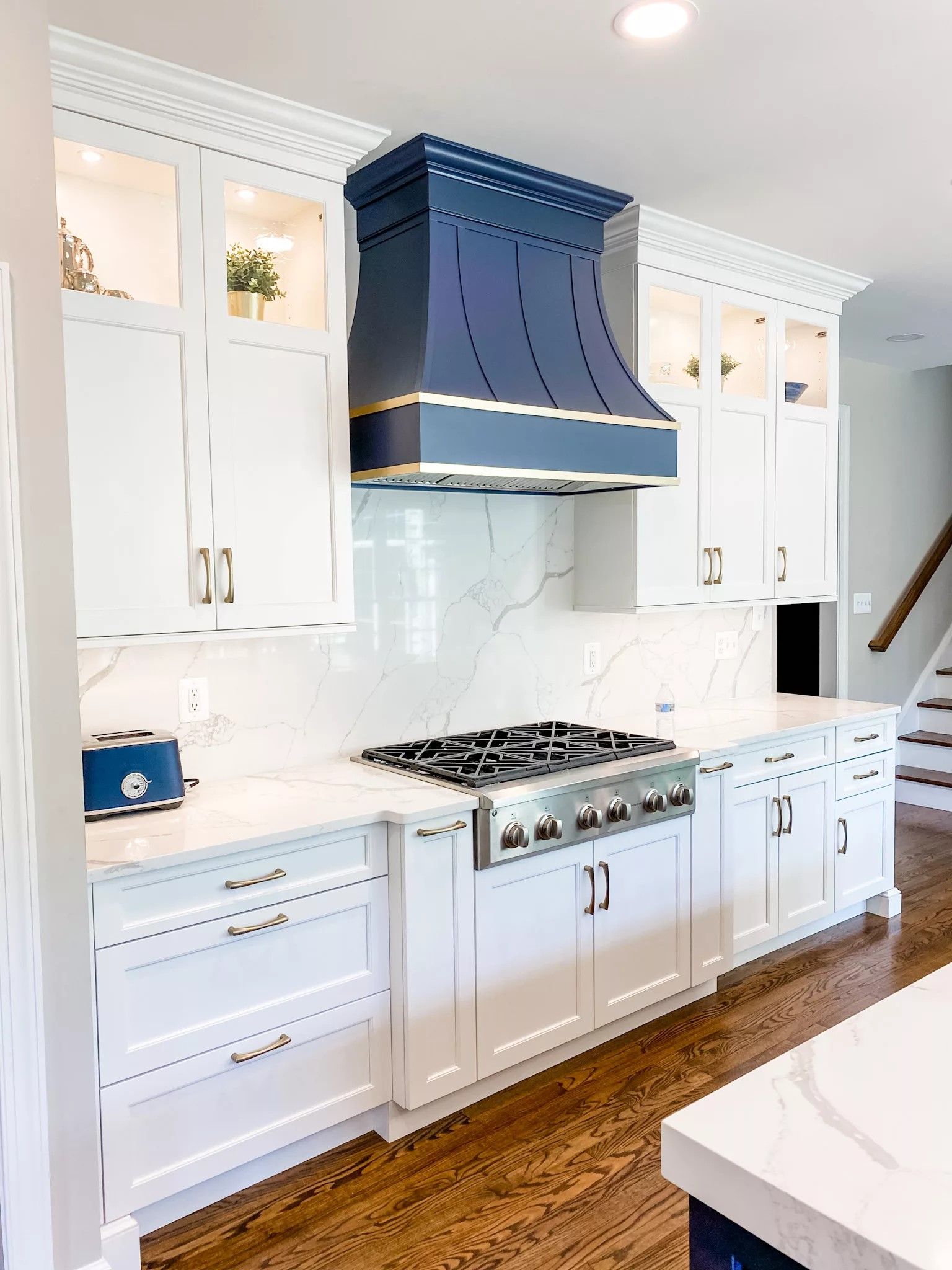 White kitchen remodel with custom navy range hood and marble backsplash